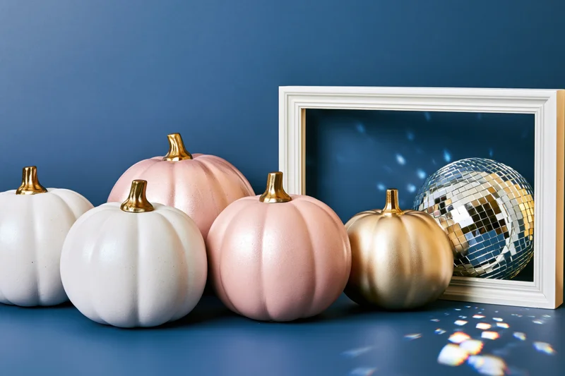 Decorative painted pumpkins and a mirrored disco ball arranged on a blue surface with a white frame in the background