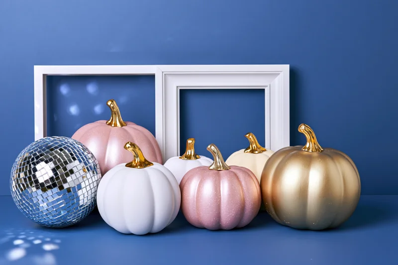 Decorative painted pumpkins and a mirrored disco ball arranged in front of white frames on a blue surface