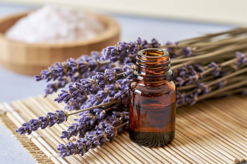Dried lavender sprigs and an amber glass bottle of essential oil arranged on a bamboo mat