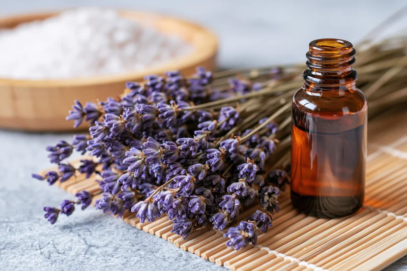 Dried lavender sprigs and an amber glass bottle of essential oil arranged on a bamboo mat