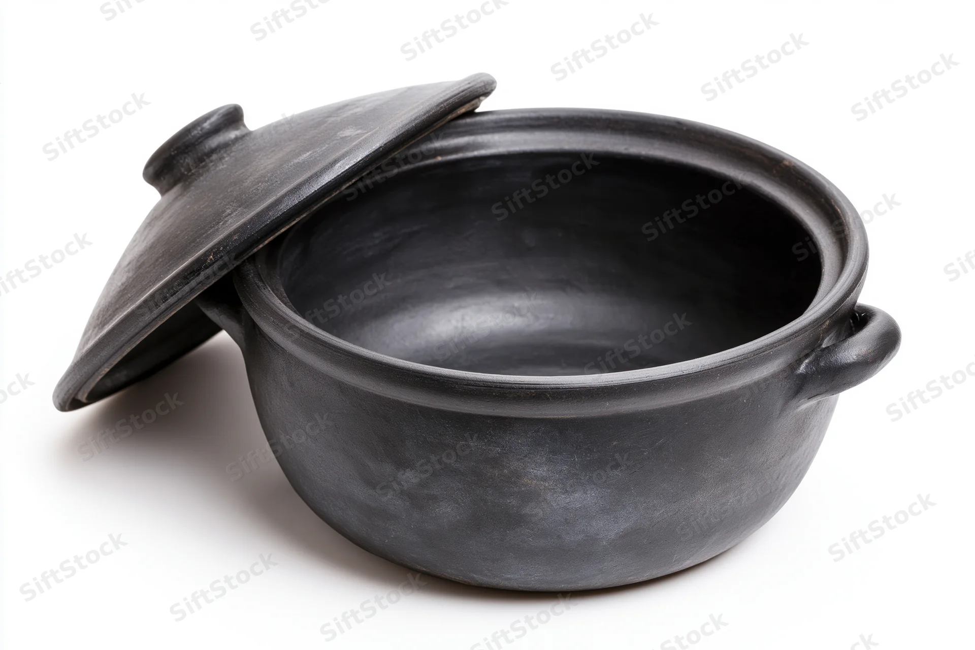 Black clay cooking pot with lid resting against it on white background