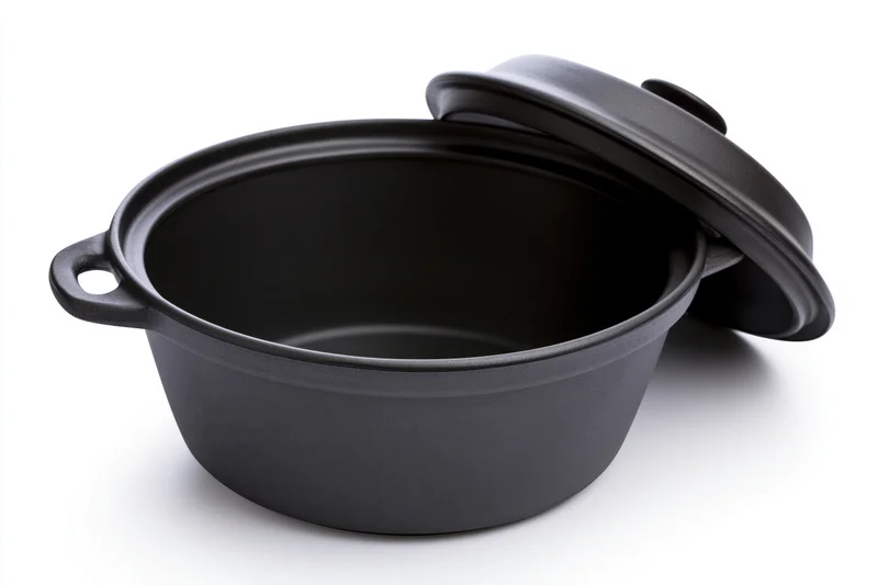 Black ceramic cooking pot with lid resting against it on white background