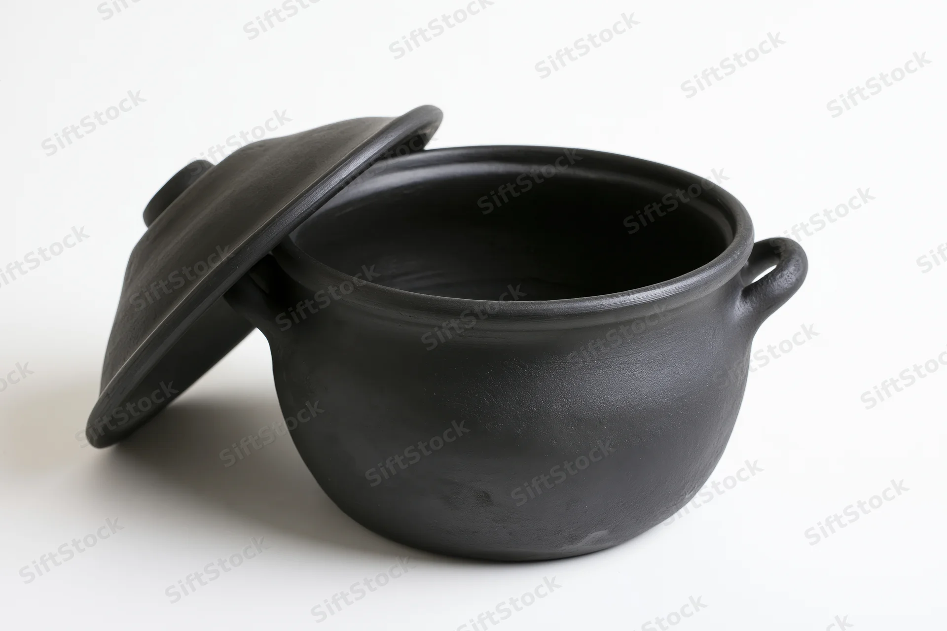 Black clay cooking pot with lid resting against it on white background
