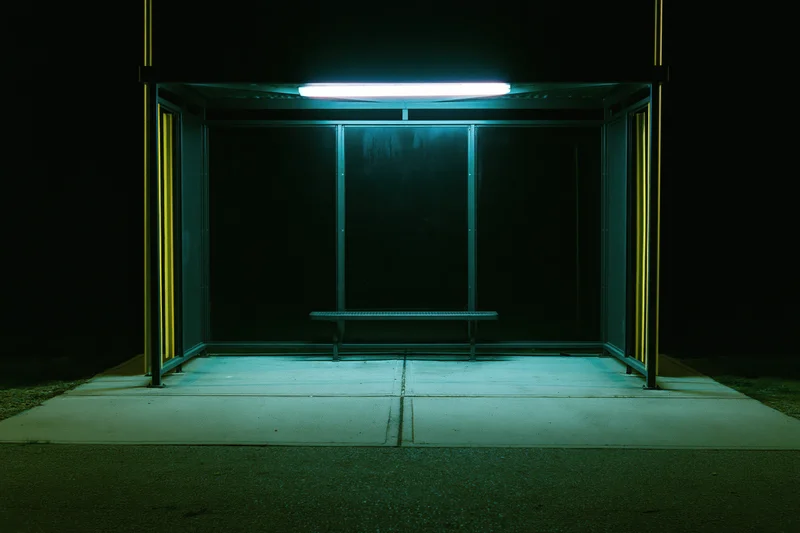 Empty bus shelter illuminated by a single fluorescent tube at night