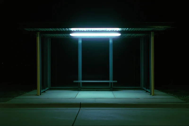 Empty bus shelter illuminated by a single fluorescent light at night