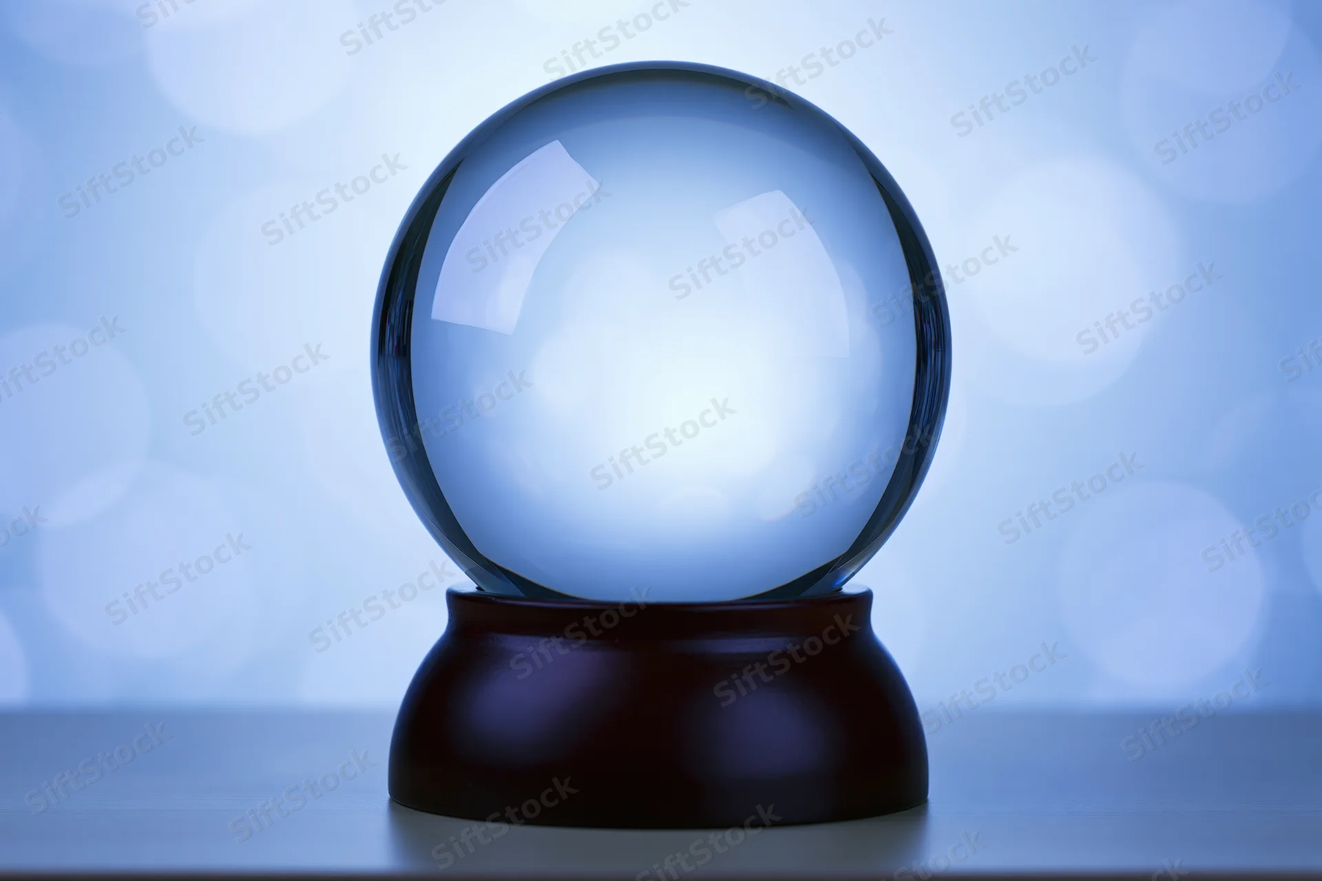Clear glass crystal globe on dark wooden base against soft blue bokeh background