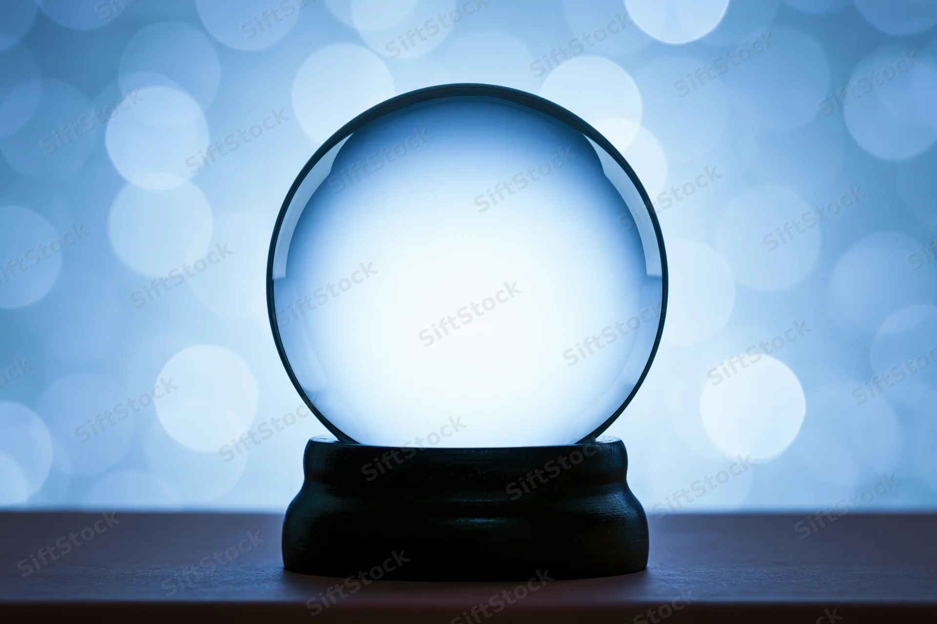 Empty glass snow globe with dark wooden base on table against blue bokeh background