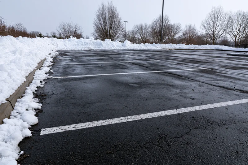 Empty parking lot with wet asphalt and snowbanks along the curb under overcast sky