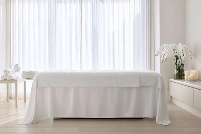 White massage table in a serene spa treatment room with orchids and candles