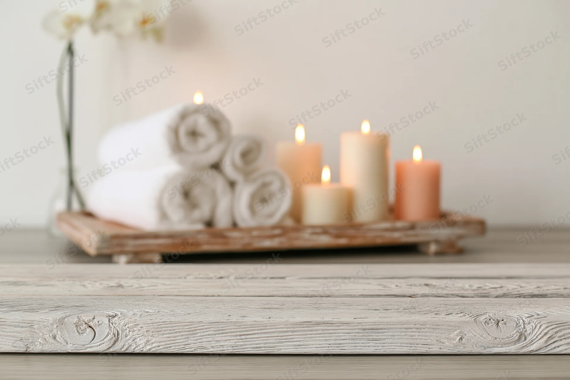 White-washed wooden surface in foreground with candles, towels and orchid on tray in background