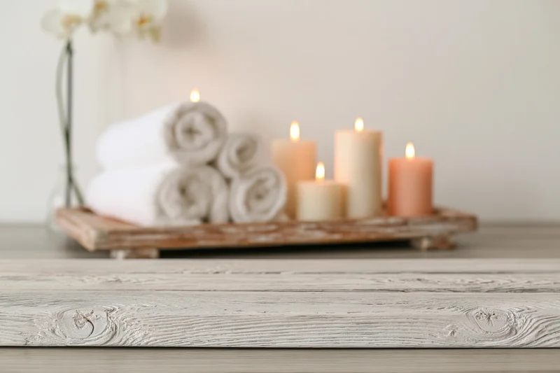 White-washed wooden surface in foreground with candles, towels and orchid on tray in background
