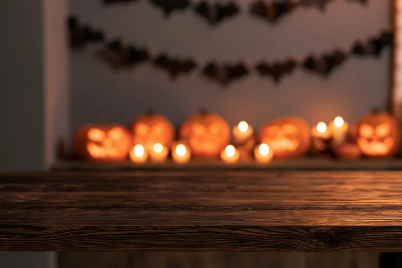 Wooden table in foreground with blurred halloween pumpkins and candles behind
