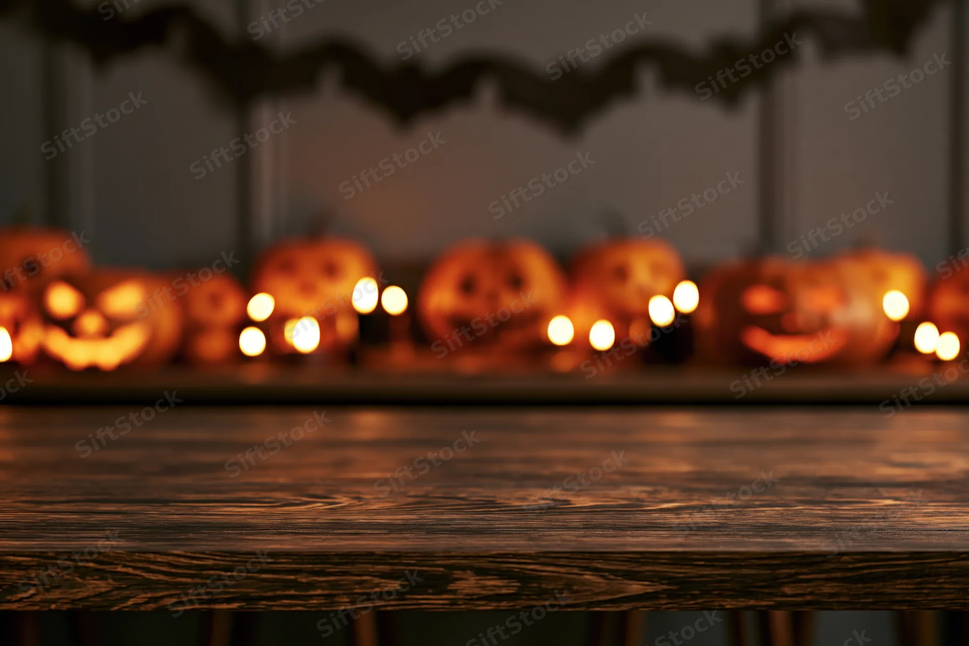 Empty wooden tabletop in foreground with blurred halloween jack-o-lanterns and candles in background