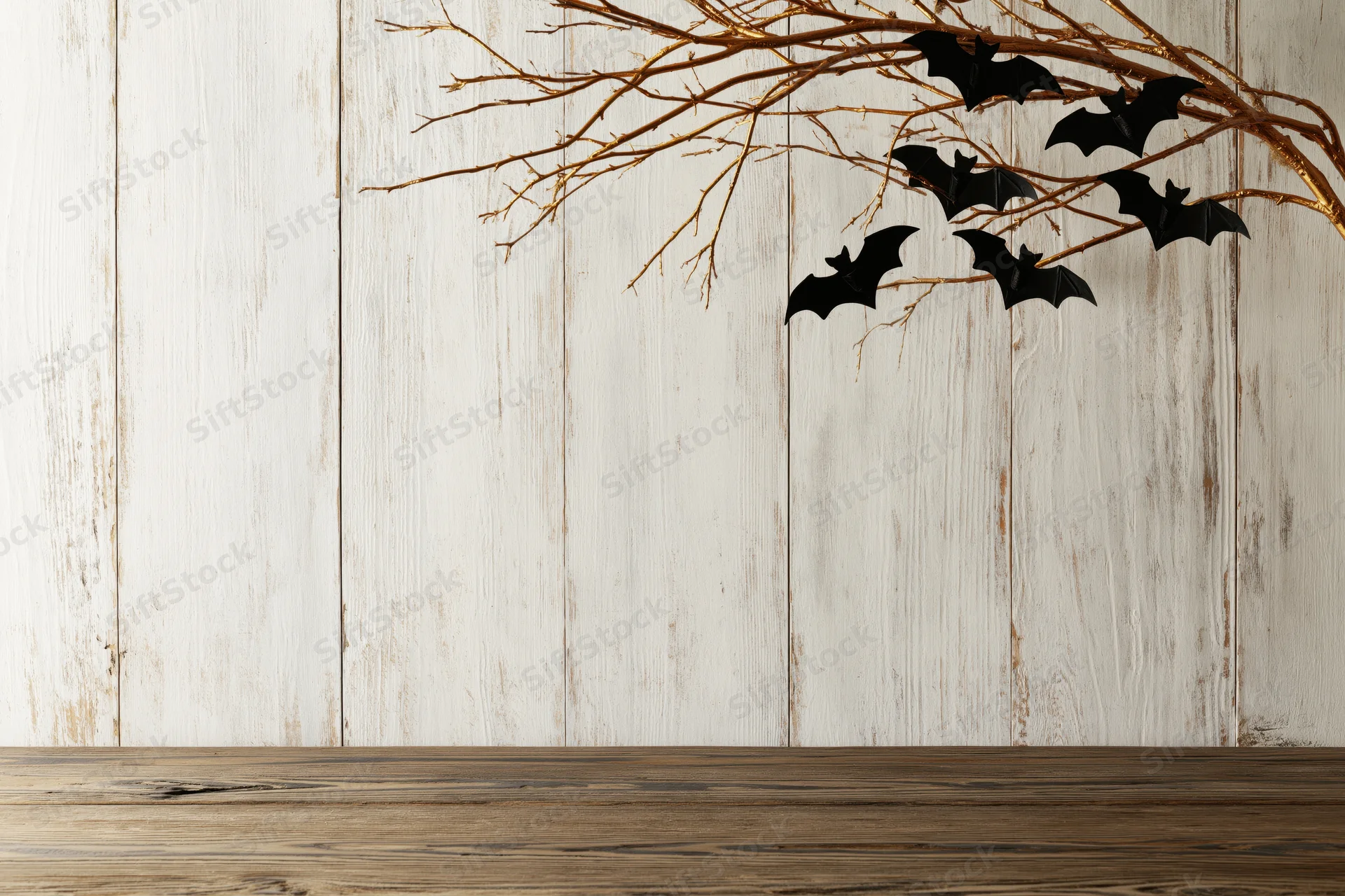 Golden branches with black bat decorations on a white wooden wall above a dark wooden tabletop