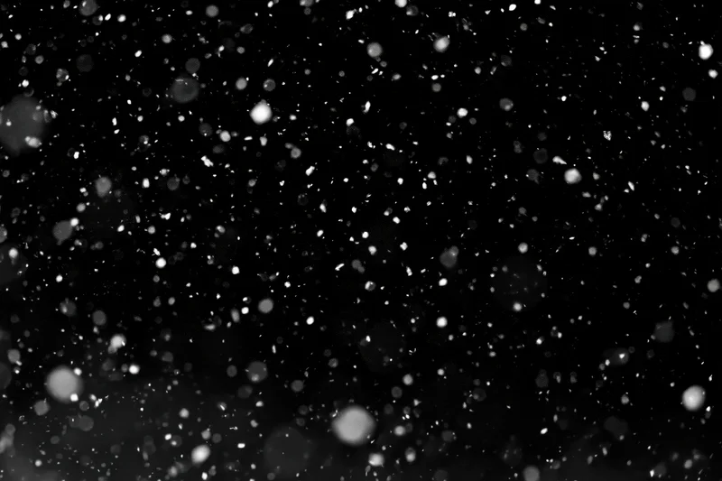 Snow particles falling mid-air against a black background