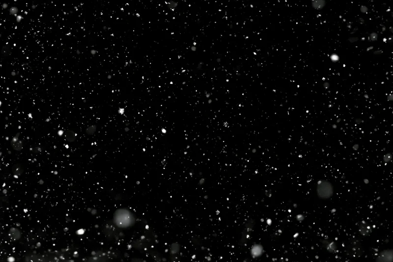 Snow particles falling midair against a black background
