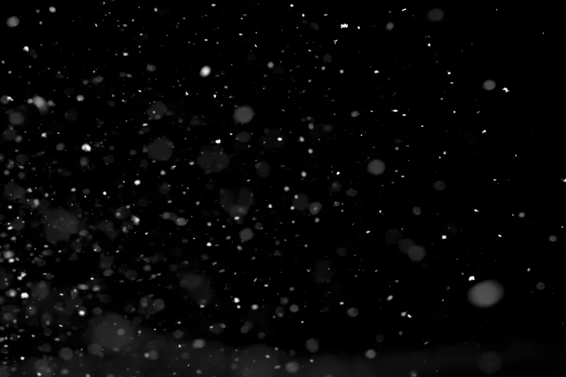 Snow particles falling mid-air against a black background