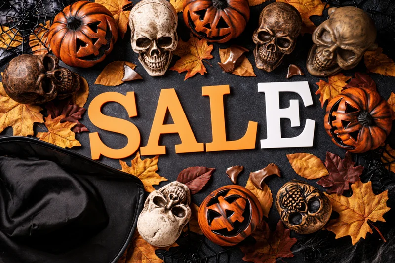 Halloween sale banner with skulls, pumpkins, and autumn leaves arranged in flat lay on dark surface