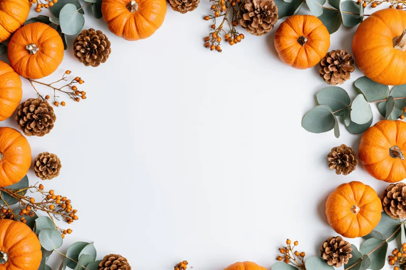 Orange pumpkins and pinecones arranged in a border around white copyspace with eucalyptus and berries