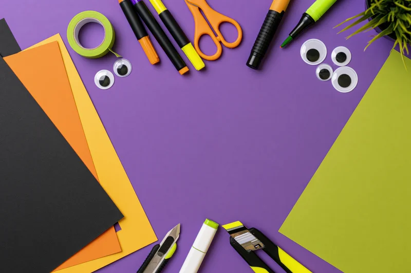 Halloween craft supplies arranged in a frame on purple background with copyspace