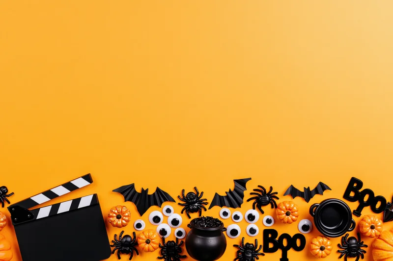 Halloween decorations and a film clapperboard arranged in a flat lay on orange background