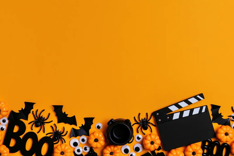 Halloween decorations and a film clapperboard arranged along the bottom of an orange background
