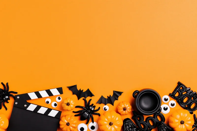 Halloween decorations and a film clapperboard arranged in a flat lay on orange background with copyspace