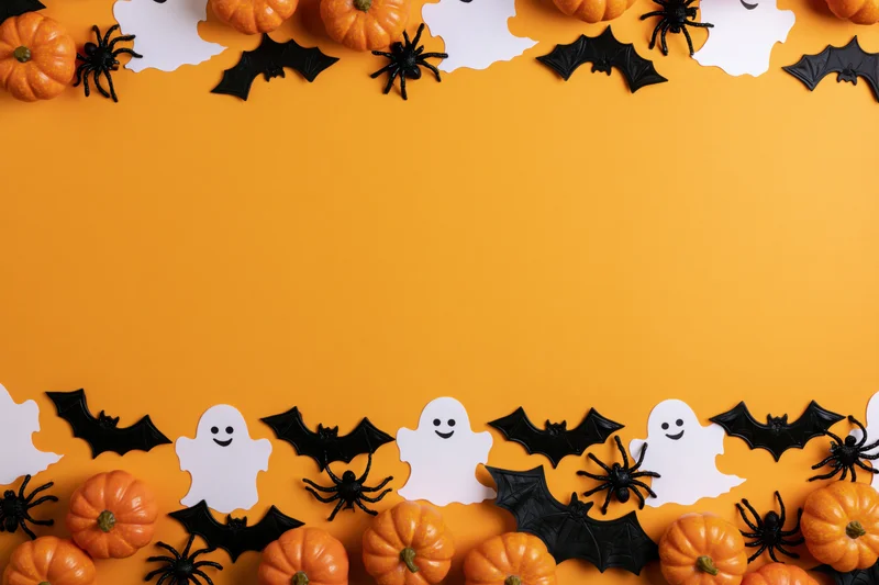 Halloween decorations arranged along the bottom and top of an orange surface with copyspace in the center