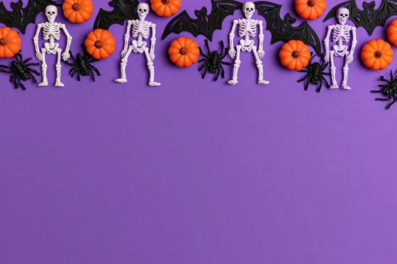 Halloween decorations including skeletons, pumpkins, spiders and bats arranged along the top edge of a purple surface