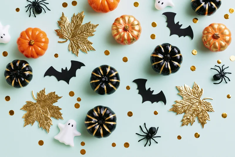 Halloween decorations including pumpkins, bats, spiders, ghosts, and gold leaves arranged in a flat lay on a pale mint blue surface