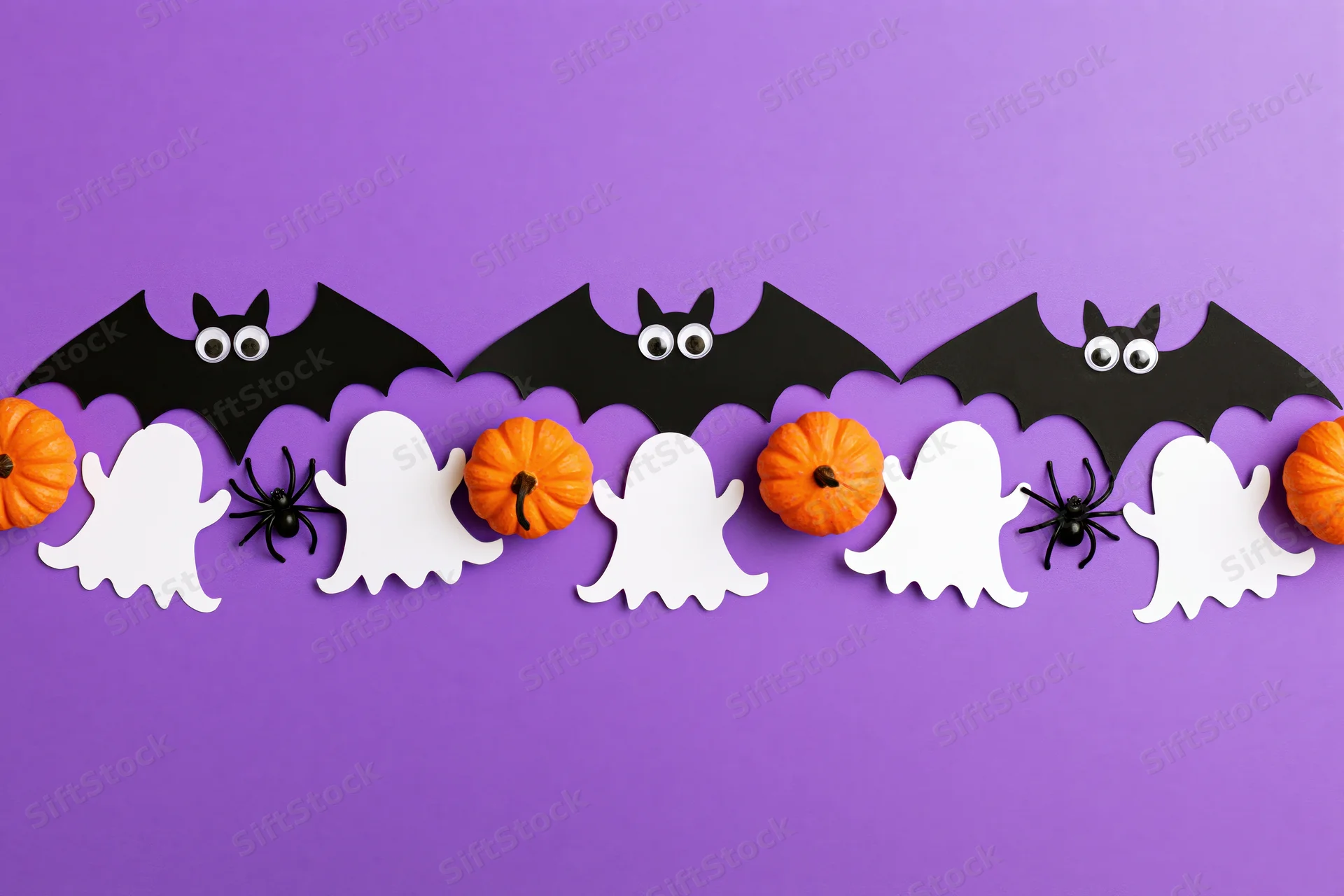 Halloween paper decorations arranged in a horizontal row on purple background