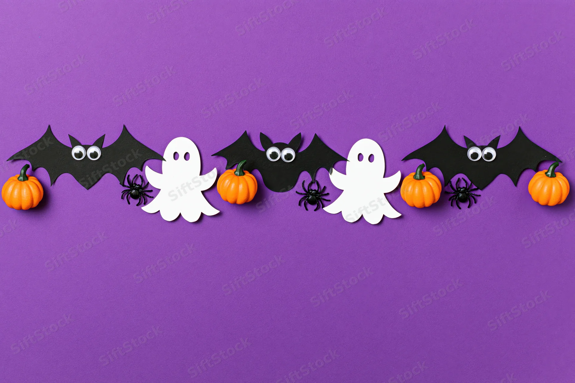 Halloween paper decorations arranged horizontally on purple background with copyspace below