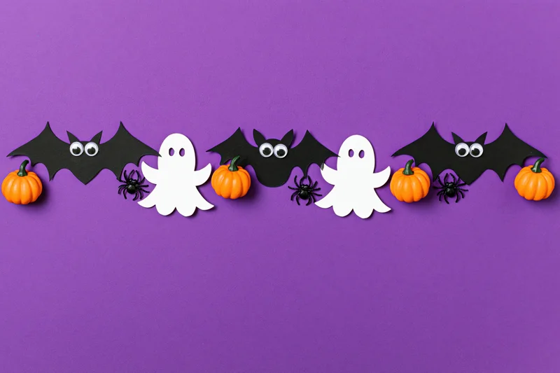 Halloween paper decorations arranged horizontally on purple background with copyspace below