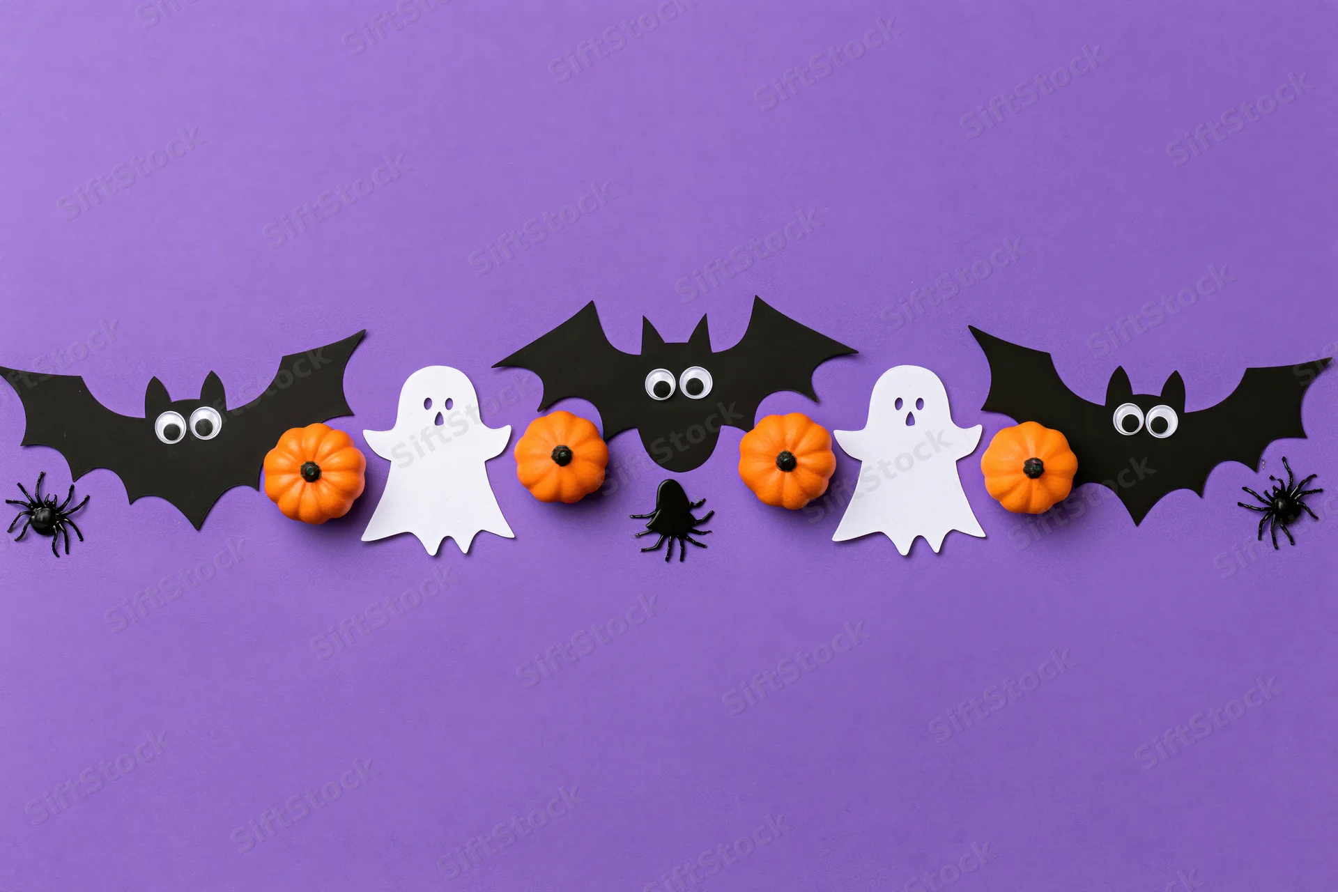 Halloween paper decorations arranged horizontally on purple background with copyspace below