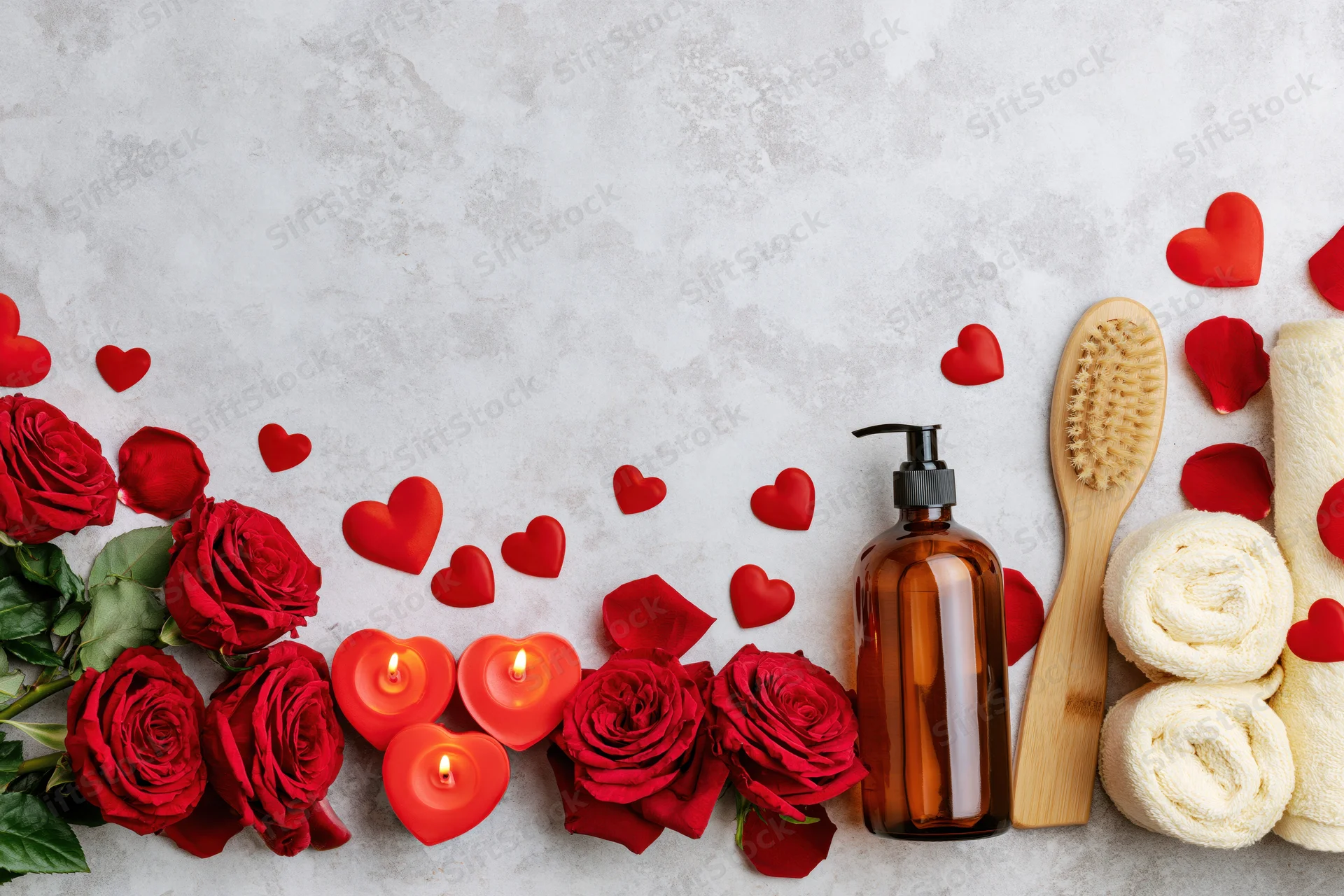 Red roses and heart-shaped candles with spa items arranged along the bottom of a light surface