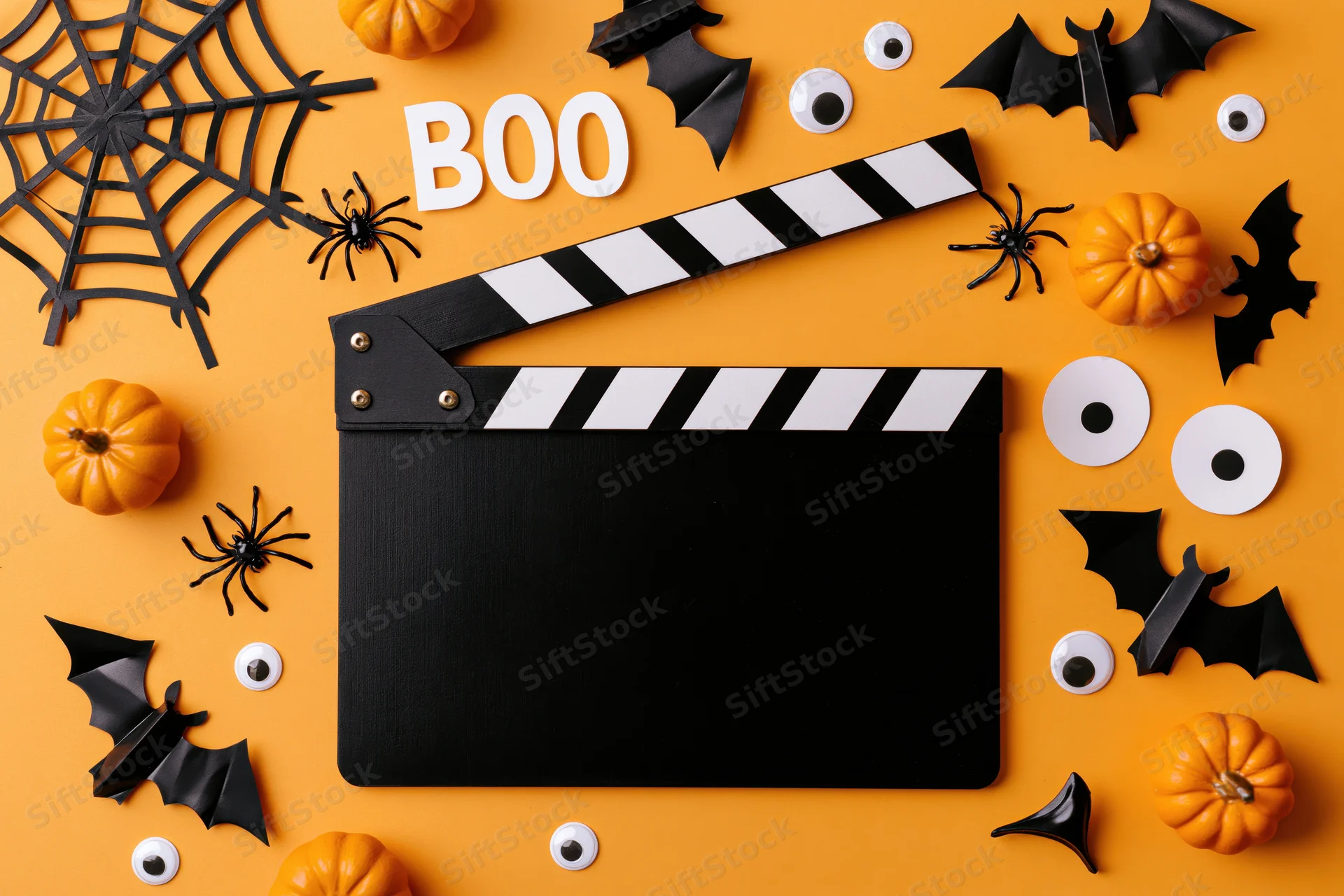 Black film clapperboard surrounded by halloween decorations on orange background
