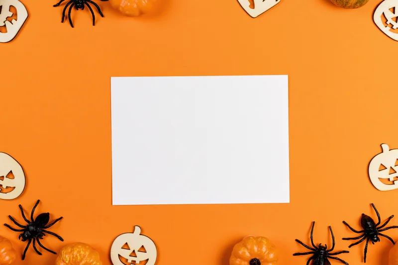 Blank white card centered on orange surface surrounded by halloween decorations