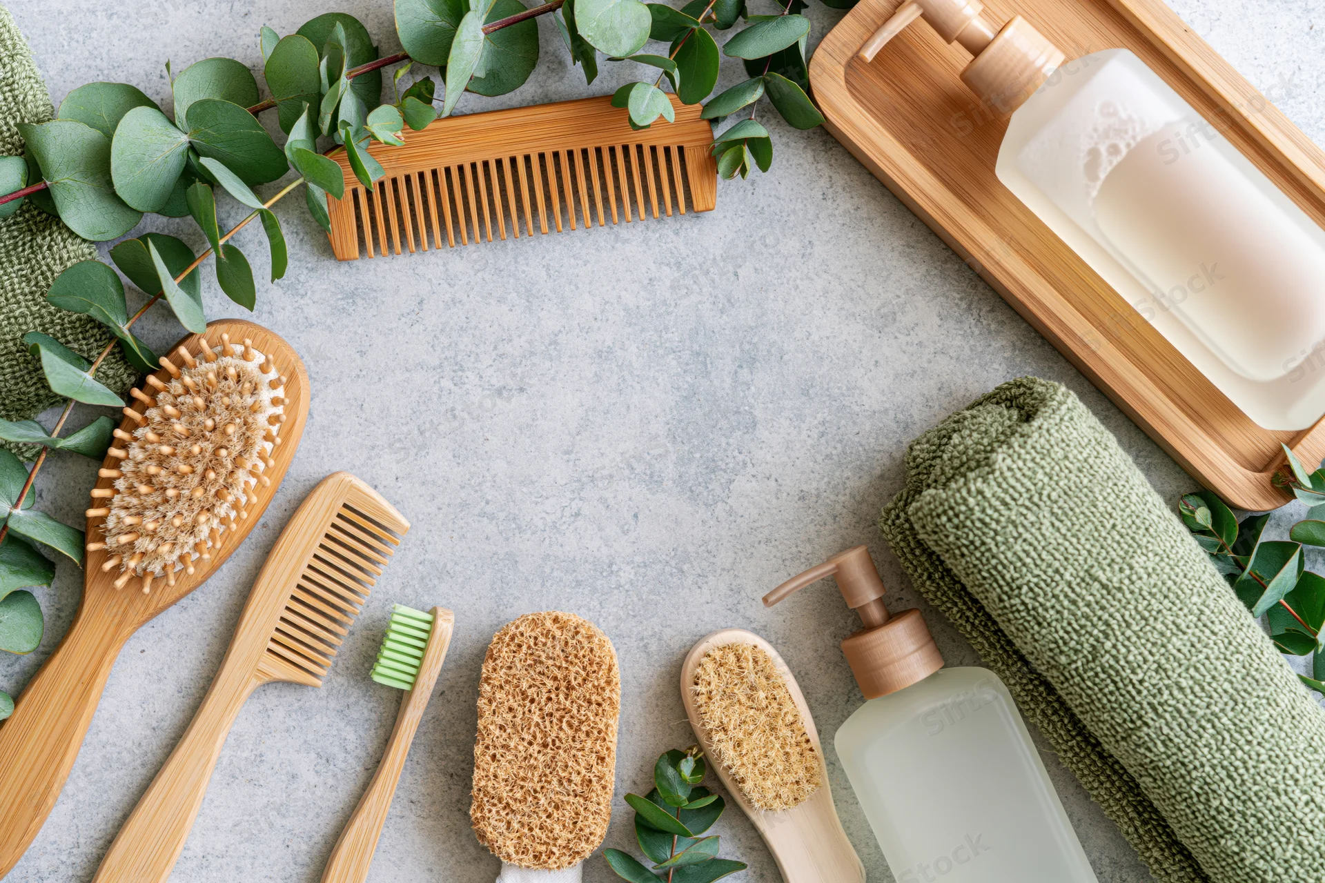 Eco-friendly bathroom accessories arranged in flat lay on gray surface with greenery and bamboo items