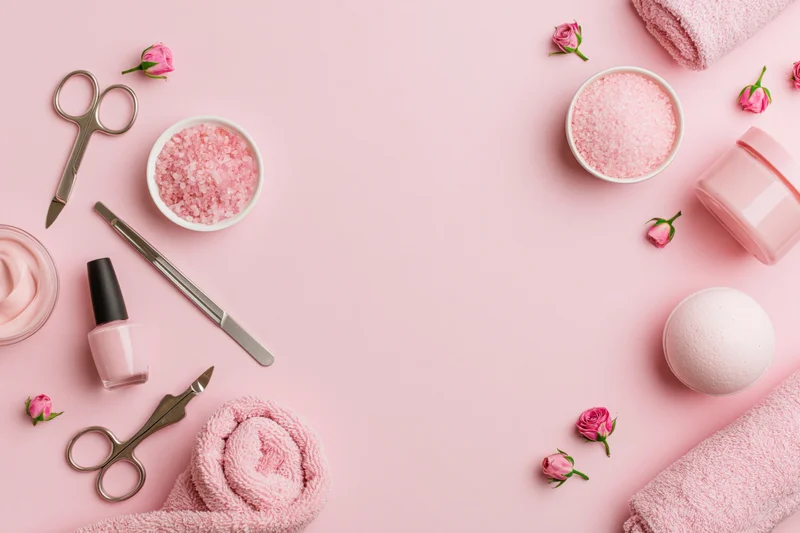 Manicure tools and beauty products arranged on a pink surface with copyspace