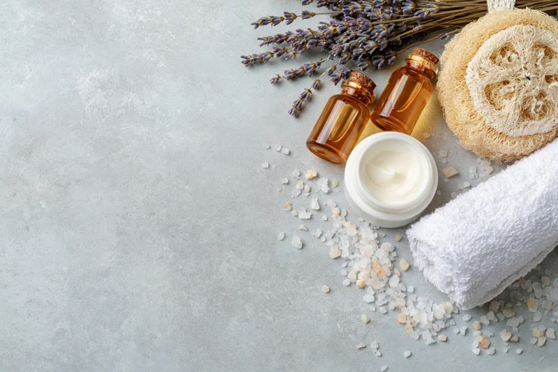 Skincare and spa products arranged on a gray surface with lavender, cream, towel and bath salt