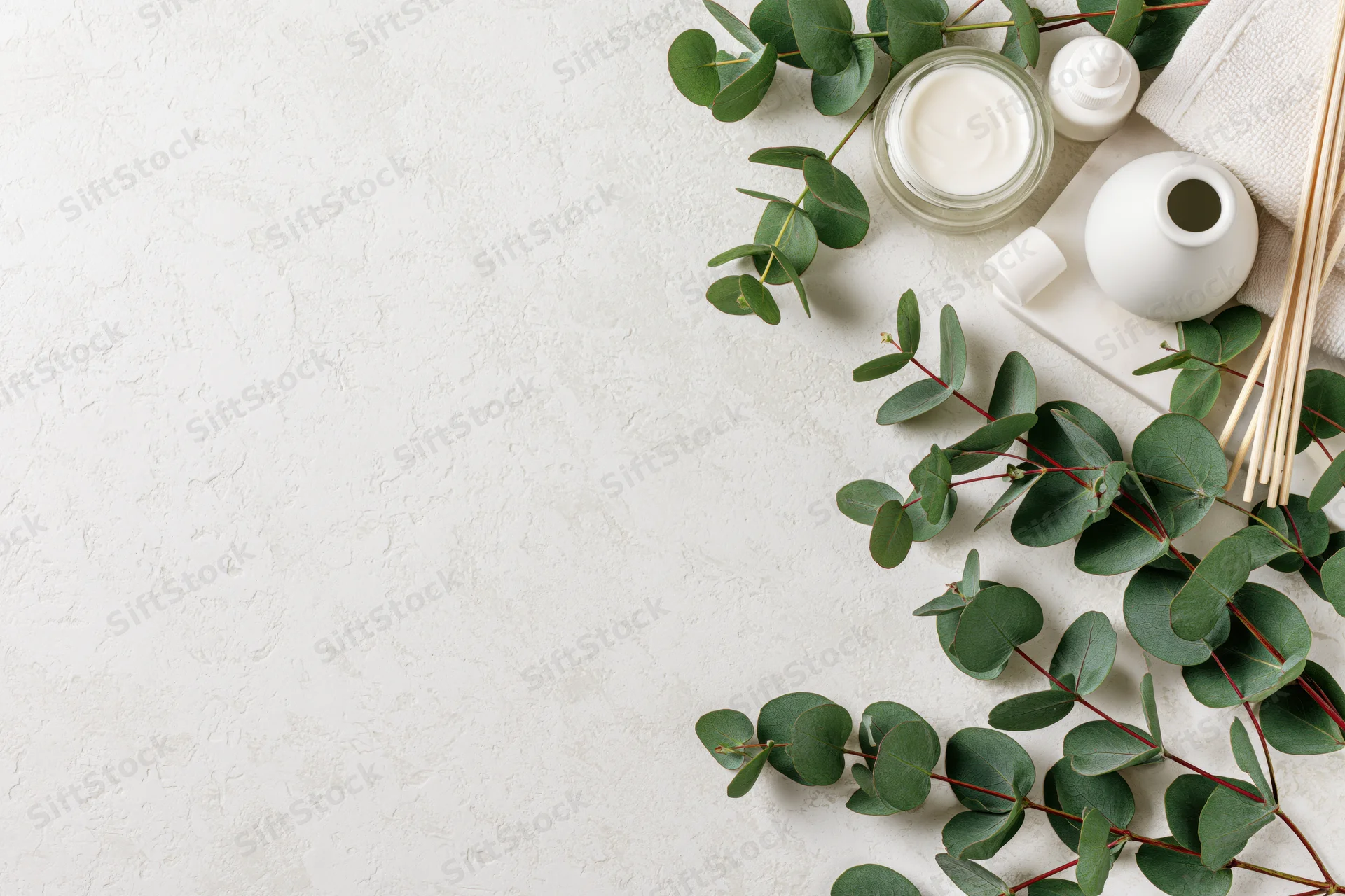 Skincare products and eucalyptus branches arranged in upper right corner on white textured surface with copyspace