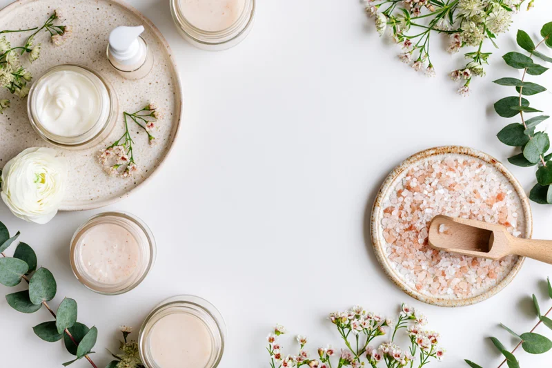 Skincare products and botanicals arranged in a flat lay on a white surface with copyspace