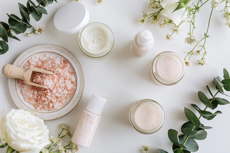 Skincare products and flowers arranged in flat lay on white surface
