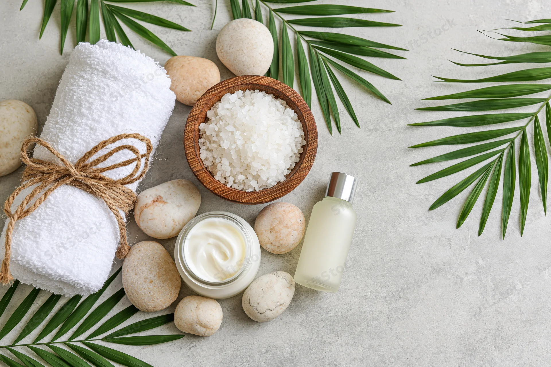 Spa and skincare products arranged with palm leaves and stones on a light gray surface