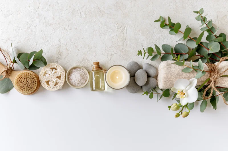 Spa and wellness items arranged in a flat lay along the top edge of a white surface with copyspace below