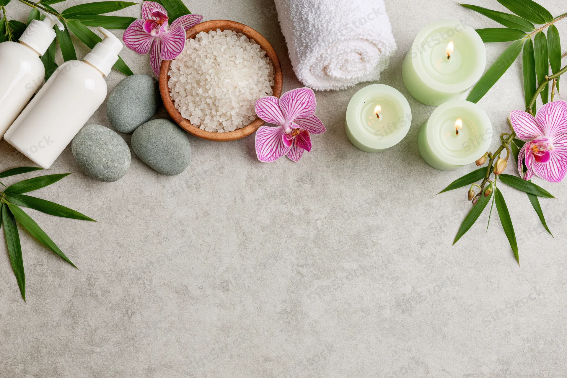 Spa wellness products arranged in flat lay with candles, orchids, bamboo, stones, towel, and salt on textured surface