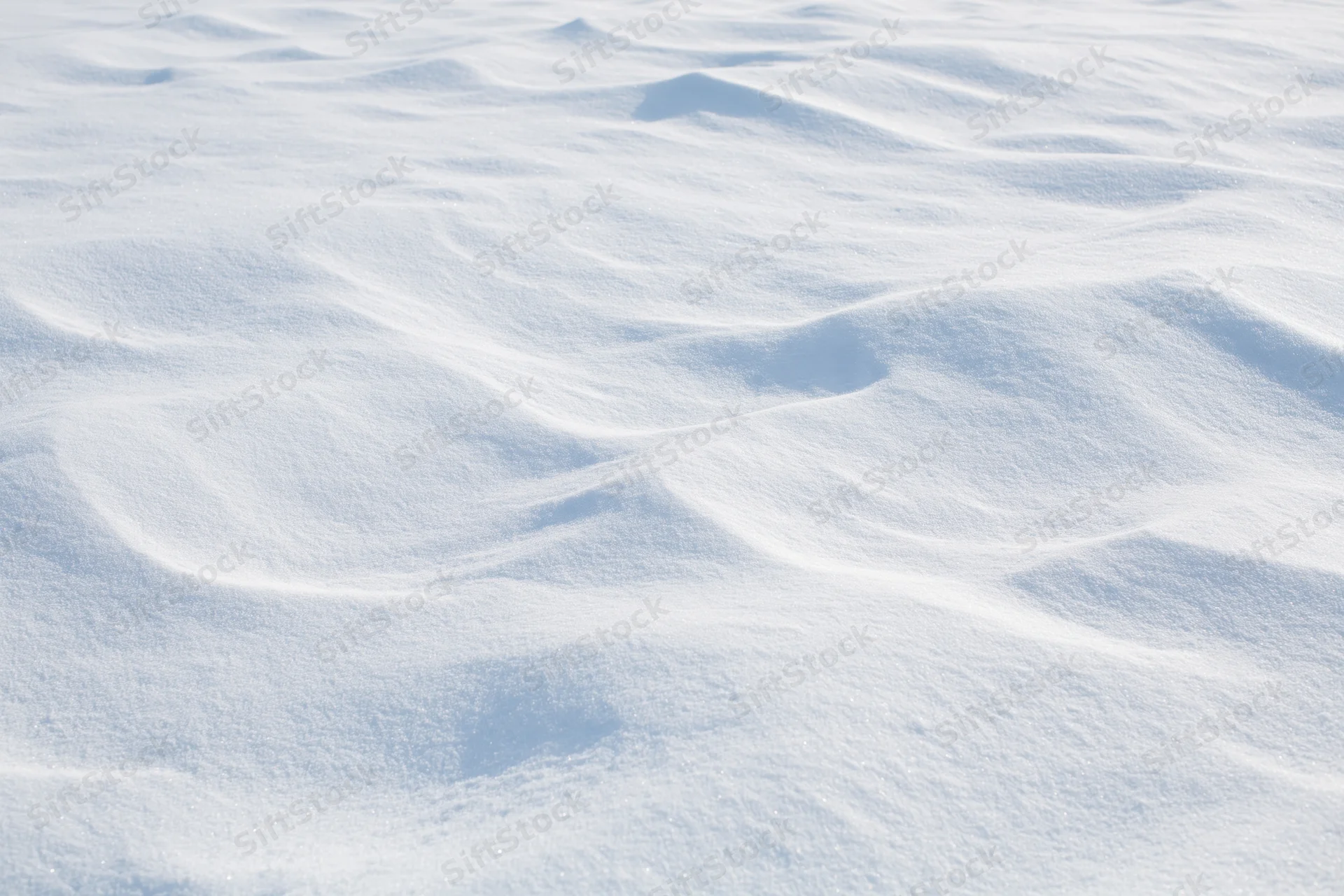 Wind-sculpted snow drifts across a flat open field under bright daylight