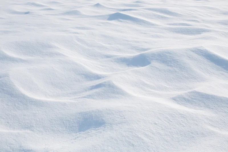 Wind-sculpted snow drifts across a flat open field under bright daylight