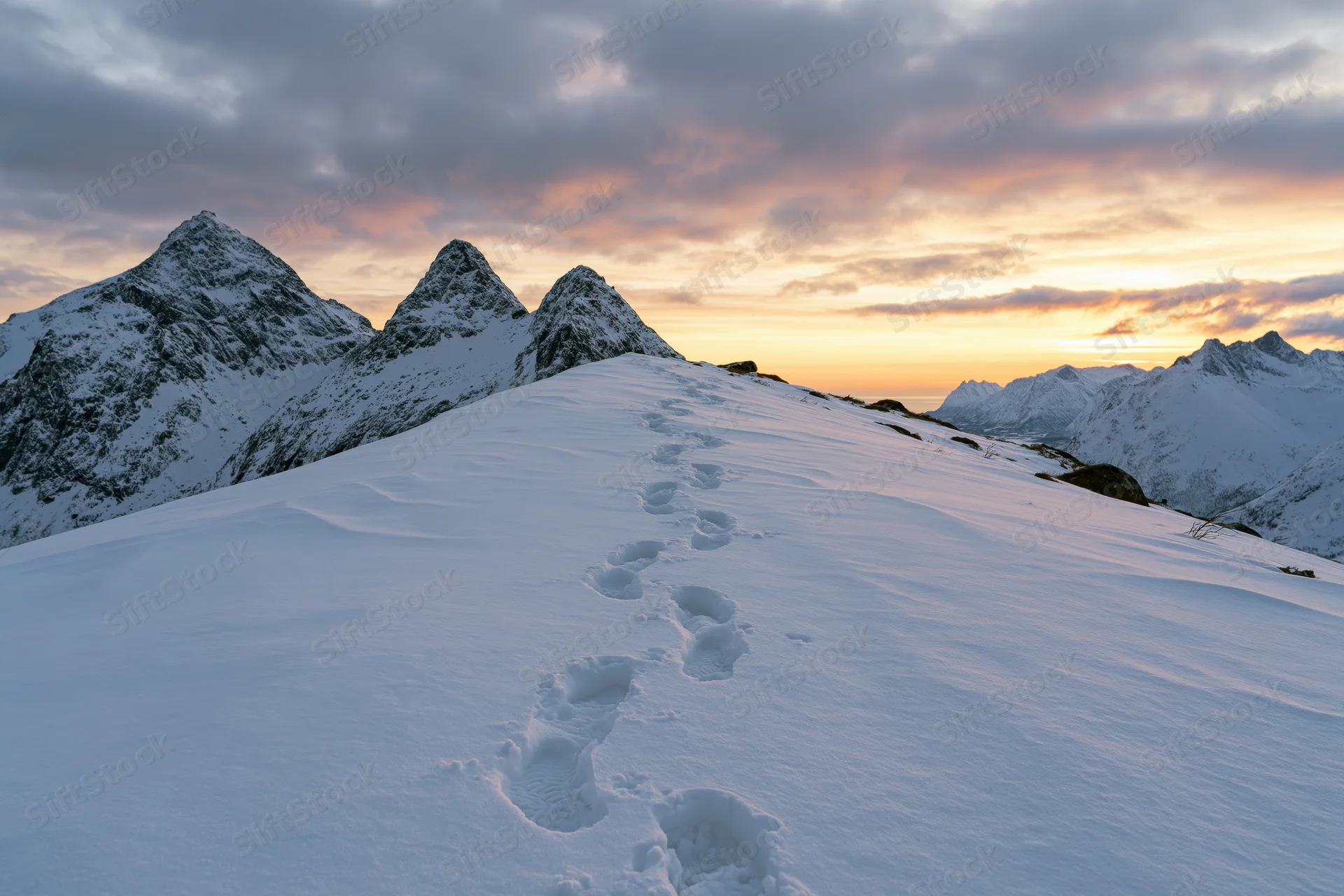 Footprints leading across a snow-covered mountain ridge at sunset
