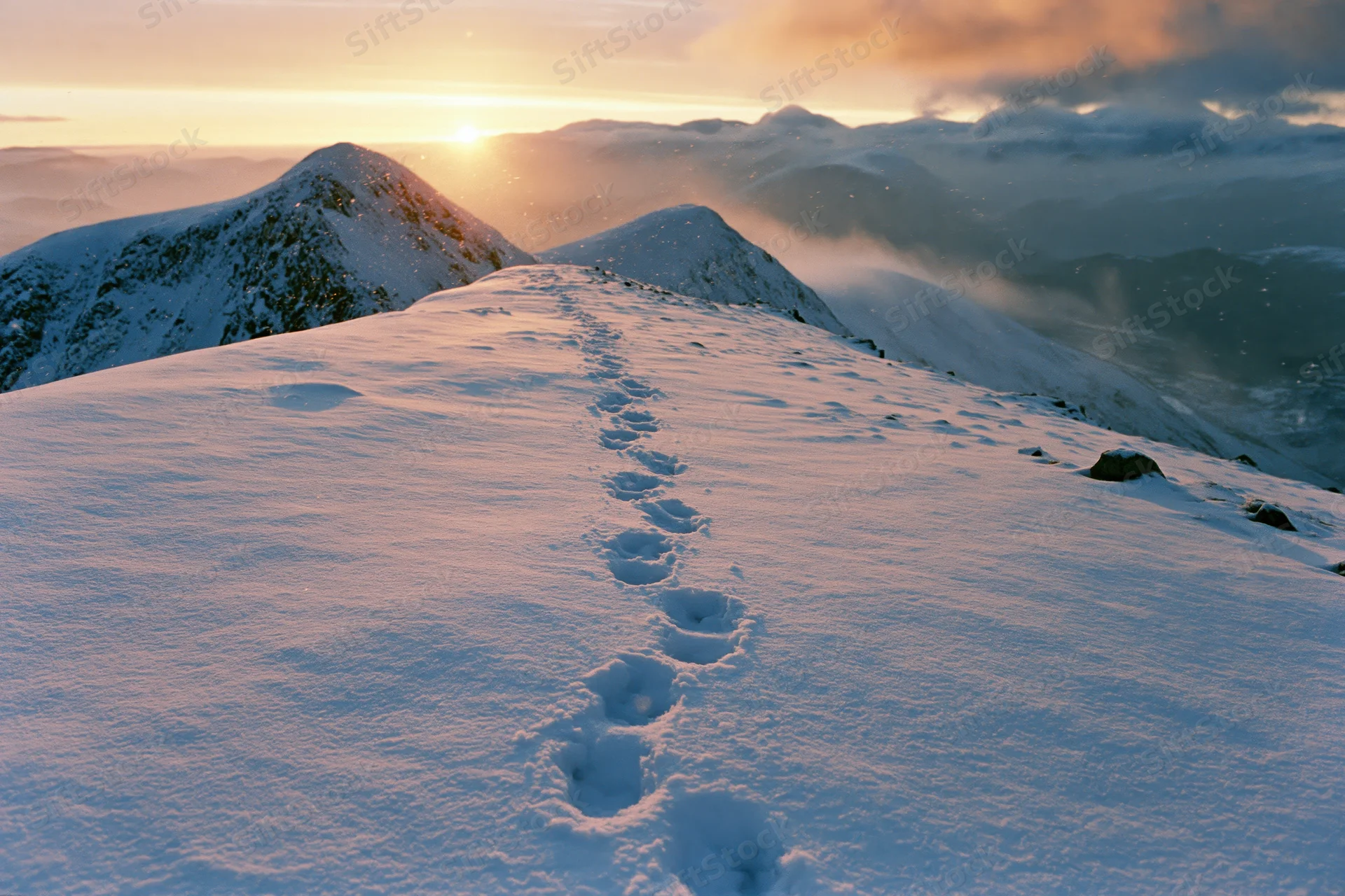 Footprints leading across a snow-covered mountain ridge at sunrise